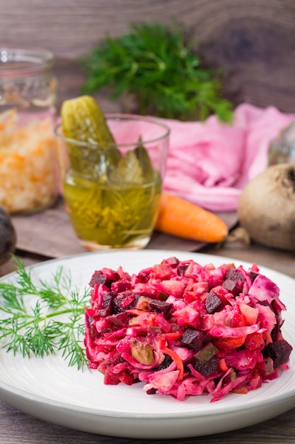Salat von gekochtem Gemüse, Sauerkraut und Gurken auf einem Teller auf einem Holztisch
