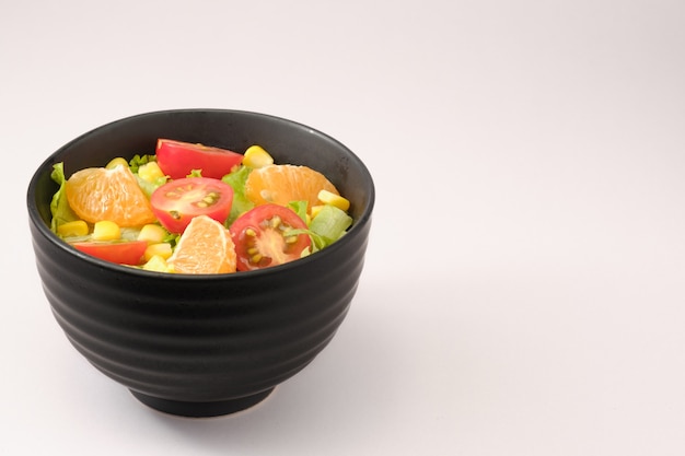 Salat von Salat und Kirschtomate, Orange, Mais in Schüssel. Konzept für eine schmackhafte und gesunde Mahlzeit. Vegetarisches Lebensmittelkonzept auf weißem Hintergrund mit Kopienraum