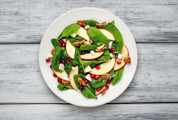 Salat von Spinat, Äpfeln, Granatapfel, Käse, Walnüssen auf einem Holzhintergrund