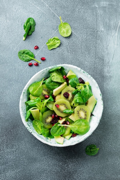 Salat von Spinatbabyblättern, Brunnenkresse, Kiwi, Avocado und Granatapfel in einer alten Keramikplatte auf einem grauen Betonhintergrund