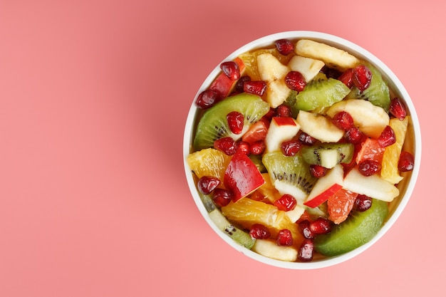 Salat von verschiedenen saftigen reifen Früchten in einer weißen Tasse auf einem rosa Hintergrund. Freiraum