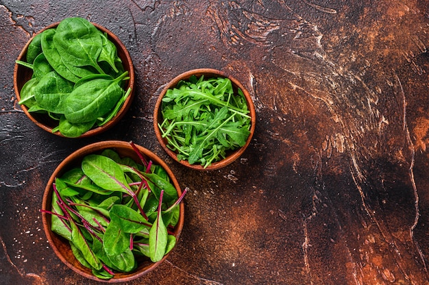 Salatblätter, Rucola, Spinat und Mangold in Holzschalen mischen