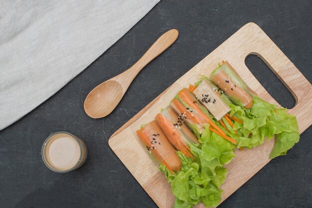 Salatbrötchen auf Holztablett mit Salatdressing und Holzlöffel und Stoffleinen auf schwarzem Holztisch