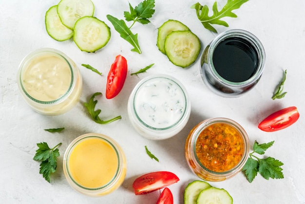 Salatdressings: Saucenvinaigrette, Senf, Mayonnaise oder Ranch, Balsamico oder Soja, Basilikum mit Joghurt. Dunkle weiße konkrete Tabelle, mit dem Grün, Gemüse für Salat. Kopieren Sie die Draufsicht des Raumes