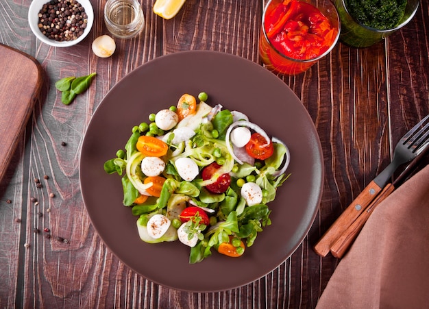 Salate mit frischen Kirschtomaten, Mozzarella, Basilikum, Rettich und anderem Grün auf dem Esstisch