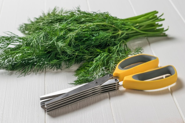 Foto salatschere und ein bündel dill auf einem weißen holztisch ein gerät zum schneiden von salat