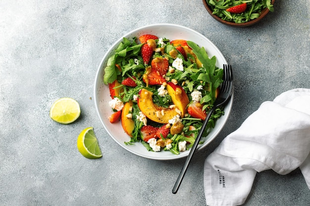 Salatschüssel mit Rucola, Erdbeere, Hüttenkäse, Nektarine und Erdnusspaste. Konzept für gesunde Ernährung