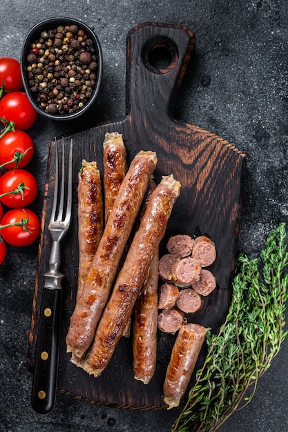 Salchicha de carne asada sobre una tabla de madera con hierbas y tomate