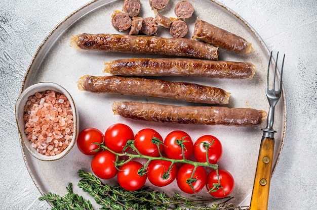 Salchicha de carne de cordero a la plancha en un plato con hierbas y tomate. Fondo blanco. Vista superior.