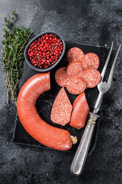 Salchicha de carne Sucuk en rodajas turcas sobre una tabla de mármol con tomillo Fondo negro Vista superior