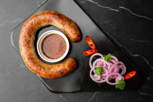 Salchicha casera jugosa al horno en un plato con salsa picante y cebolla marinada sobre fondo de mármol