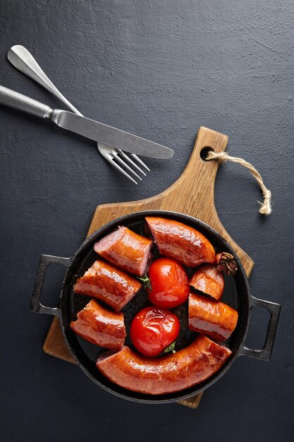 Foto salchicha de cerdo frita en rodajas y tomates asados en una sartén de hierro fundido sobre una mesa de piedra negra vista superior vertical con espacio para copiar