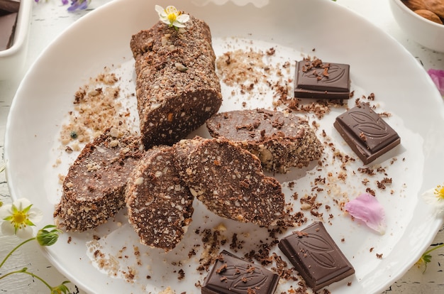 Salchicha de chocolate vegetariana hecha de nueces, cacao, galletas en una placa blanca de cerca