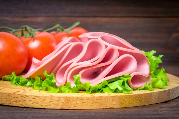 Salchicha cortada con la ensalada en un tablero de madera redondo.