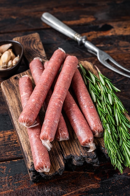 Foto salchicha cruda de ternera y cerdo en tabla de cortar antigua con tenedor de carne vintage. fondo de madera oscura. vista superior.