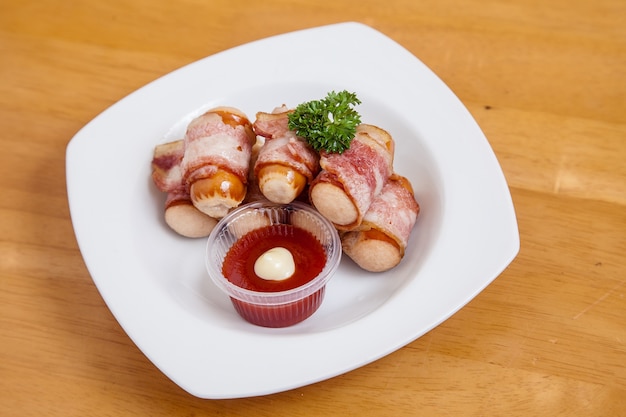 salchicha envuelta en tocino y salsa de tomate en el plato blanco en la mesa de madera