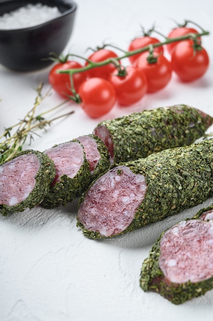 Salchicha de fuet tradicional en hierbas con ingredientes sobre fondo blanco con textura.