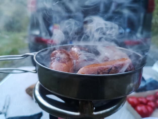 Salchicha humeante frita mientras se cocina en la naturaleza y el bosque en bushcrafting