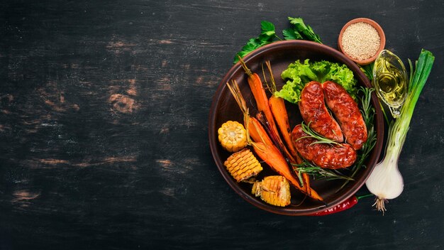 Salchicha a la parrilla Maíz y zanahorias al horno Sobre un fondo de madera Vista superior Espacio de copia