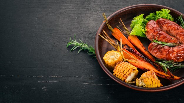 Salchicha a la parrilla Maíz y zanahorias al horno Sobre un fondo de madera Vista superior Espacio de copia