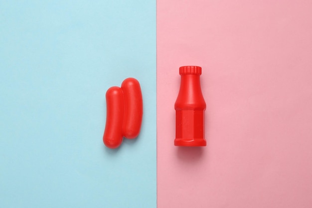 Salchicha de plástico de juguete con ketchup en un fondo pastel rosa azul Vista superior