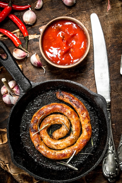 Salchicha en una sartén con salsa de tomate y ajo. Sobre un fondo de madera.