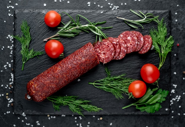 Salchicha seca de salami con romero fresco y especias en una piedra