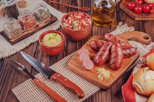 Salchichas brasileñas a la parrilla sobre la plancha de madera con pan, ensalada, farofa e ingredientes