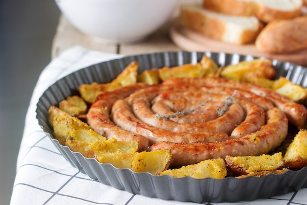 Salchichas de carne aromática con patatas, ensalada y vino en una mesa de madera.