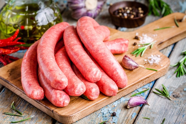 Salchichas caseras crudas en tabla de cortar con romero y ajo en mesa rústica