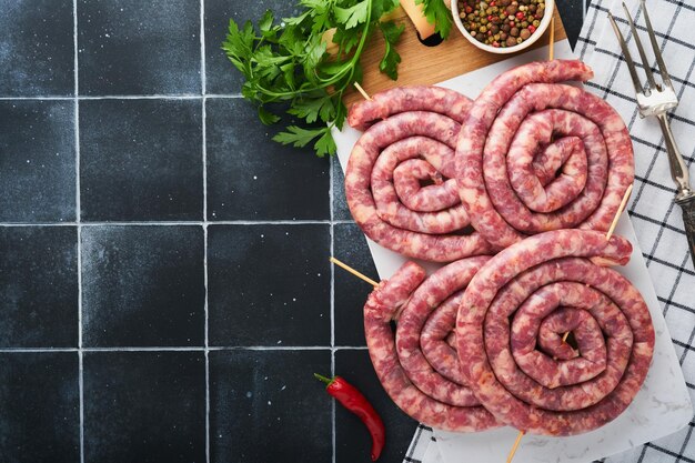 Salchichas de cerdo crudas en espiral Salchichas de cerdo frescas deliciosa espiral retorcida para barbacoa en soporte blanco con especias y hierbas para la cena de la fiesta de octubre sobre fondo gris Vista superior Conjunto de Oktoberfest