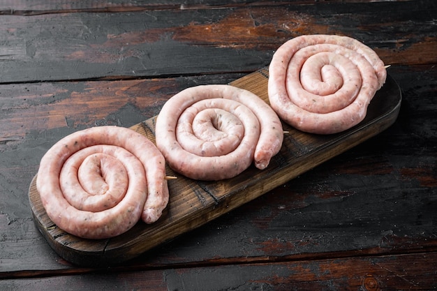 Salchichas de cerdo en espiral crudas tradicionales sobre fondo de mesa de madera oscura