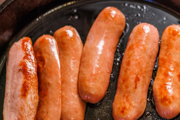 Las salchichas cortadas a la mitad se fríen en aceite en una sartén de hierro fundido negro