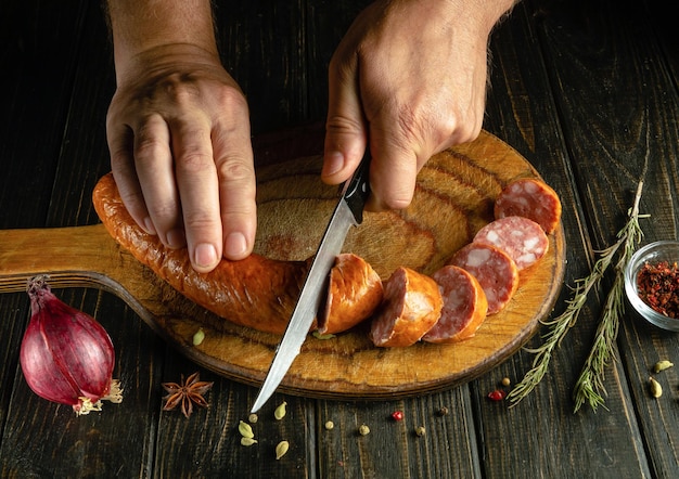 Salchichas cortadas en una tabla de cortar de madera en la cocina del restaurante por las manos del chef Idea para preparar un refrigerio o una comida rápida