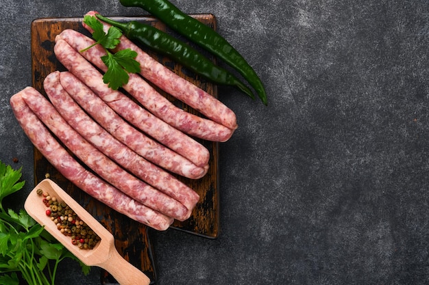 Salchichas crudas Bratwurst o salchichas con ingredientes en una tabla de cortar con especias sobre un fondo de piedra con espacio para copiar Fondo de cocina de alimentos Vista superior