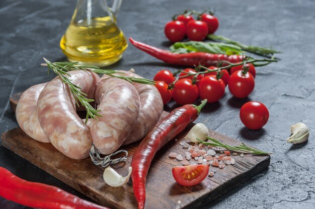 Salchichas crudas en tabla de cortar, chile y tomates, fondo rústico de cocina, enfoque selectivo