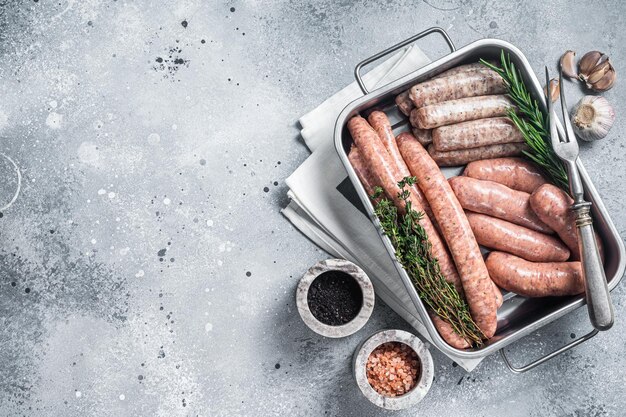 Salchichas crudas variadas Salchichas de carne picada de pollo y cordero de cerdo de res en una bandeja de cocina de acero con hierbas Fondo gris Vista superior Espacio de copia