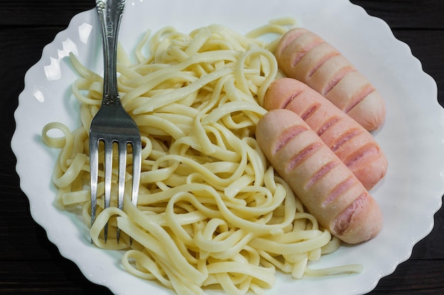 Salchichas y espaguetis en plato blanco sobre fondo de madera oscura.