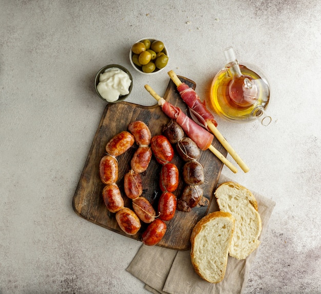 Foto salchichas españolas asadas en la tabla de cortar - butifarra blanca, chorizo, morcilla de cebolla, jamón y ajo alioli