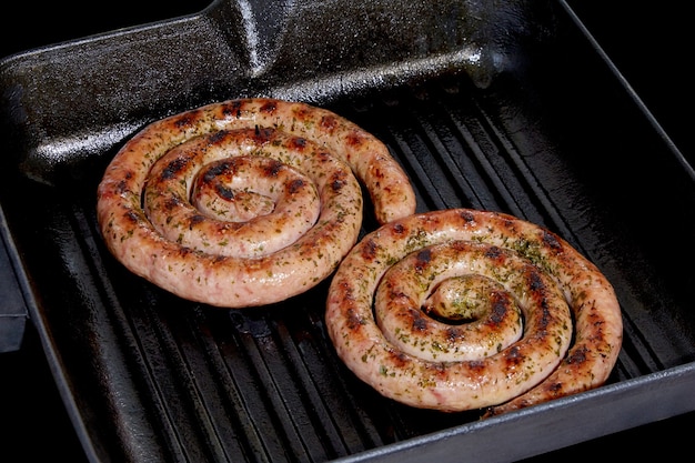 Salchichas en espiral en una parrilla sobre un fondo oscuro.