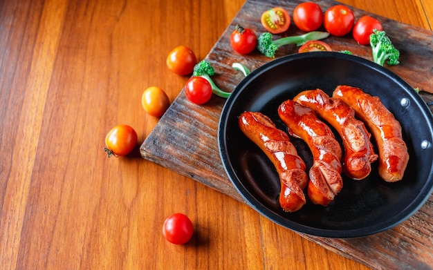 Salchichas fritas en una sartén con tomates y brócoli