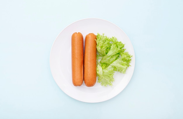 Salchichas hervidas en placa de cerámica blanca con verde, desayuno matutino, vista superior, diseño