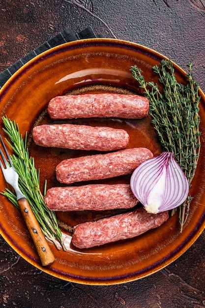 Salchichas de kebabs de carne cruda kofta en un plato con hierbas. Fondo oscuro. Vista superior.