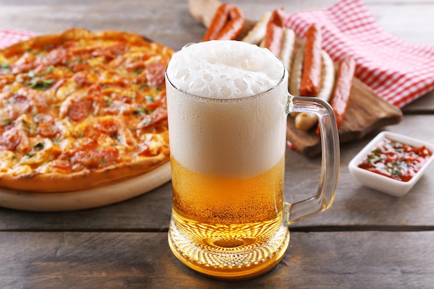 Salchichas a la parrilla deliciosa pizza y vaso de cerveza en la mesa de madera de cerca