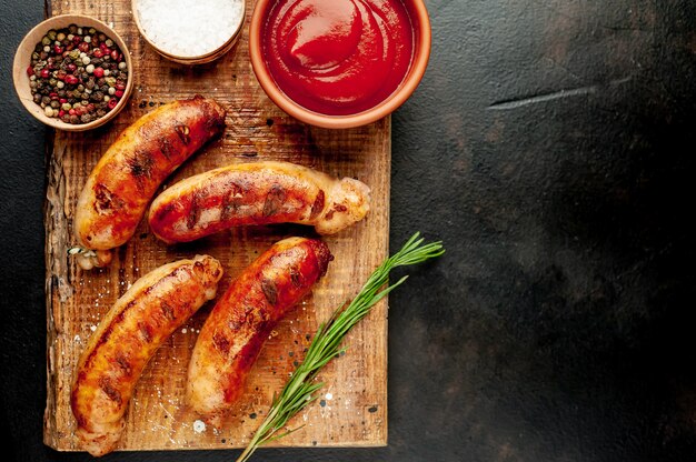 Salchichas a la parrilla con especias, salsa de tomate y romero sobre una mesa de piedra, listas para comer