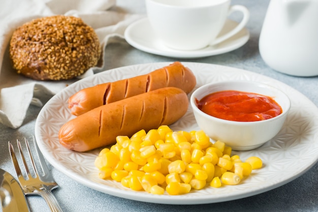 Salchichas a la parrilla, maíz enlatado y salsa de tomate en un plato