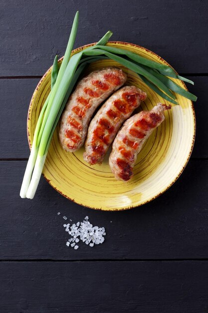 Salchichas a la parrilla en plato amarillo Plato con plato de carne sobre fondo oscuro Salchichas calientes con especias y cebolletas Vista superior Copiar espacio