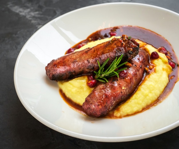 Salchichas a la parrilla con puré de papas en un plato blanco sobre un fondo de piedra