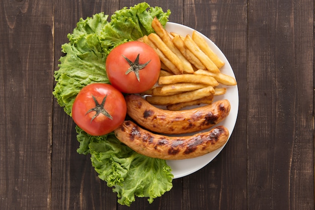 Salchichas a la parrilla y verduras con papas fritas sobre fondo de madera