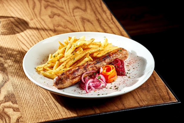 Salchichas a la plancha con patatas fritas en un plato blanco sobre una mesa de madera. Currywurst